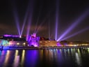 Nachts beleuchtete Gebäude mit Lichtsäulen am Fluss.