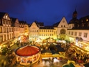 Abendlicher Weihnachtsmarkt auf einem Platz mit Lichtern und Menschen.