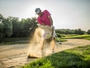 Golfer im rosa Hemd schlägt aus einem Sandbunker.