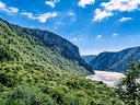 Aussicht auf Fluss und bewaldete Berge unter blauem Himmel.