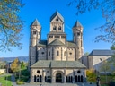 Romanische Kirche mit drei Türmen unter blauem Himmel.