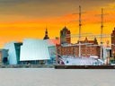 Schiff vor moderner Architektur und Altstadt im Sonnenuntergang.