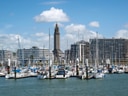 Hafen mit Segelbooten vor modernen Gebäuden und Turm.