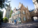 Mittelalterliche Gebäude mit Kirche im Hintergrund, zwei Personen gehen spazieren.