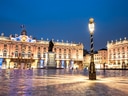 Platz mit beleuchtetem Gebäude und Statue bei Nacht.