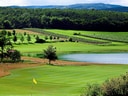 Golflandschaft mit Teich und bewaldeten Hügeln.