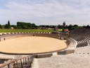Freilichtarena mit steinernen Sitzreihen und Bäumen im Hintergrund.