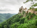 Historische Burg auf einem bewaldeten Hügel mit Talblick.
