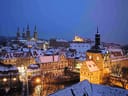 Verschneite Stadtansicht mit beleuchteten historischen Gebäuden bei Dämmerung.