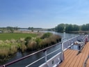Aussicht vom Boot auf Fluss, Wiesen und Bäume.