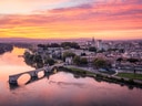 Luftaufnahme einer Stadt am Fluss mit alter Brücke bei Sonnenuntergang.