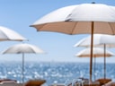 Tisch mit Geschirr und Gläsern unter Sonnenschirmen am Meer.
