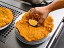 Hand legt Zitronenscheibe auf Wiener Schnitzel auf einem Tellerstapel ab.