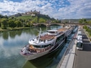 Flusskreuzfahrtschiff am Ufer mit Burg im Hintergrund.