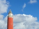 Roter Leuchtturm und Haus unter blauem Himmel.