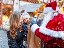 Kind und Frau treffen Weihnachtsmann auf verschneitem Weihnachtsmarkt.