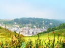 Blick auf eine Stadt in einem Tal, umgeben von grünen Hügeln und einem Golfplatz im Vordergrund.