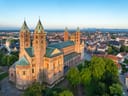 Luftaufnahme einer grossen Kathedrale mit Türmen über einer Stadtlandschaft bei klarem Himmel.