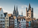 Bunte Häuserzeile und Dom in Köln bei Tageslicht.