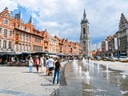 Hauptplatz mit historischen Gebäuden, Springbrunnen und Turm im Hintergrund.