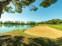 Golfplatz mit Sandbunker und See unter blauem Himmel.