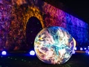 Beleuchtete bunte Kugel vor bemalter Wand bei Nacht.