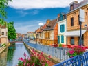 Bunte Häuser entlang eines Kanals mit Brücke und Blumen.