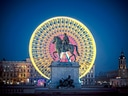 Reiterstatue vor beleuchtetem Riesenrad bei Nacht.