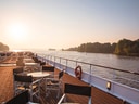 Sonnendeck eines Schiffes auf einem Fluss mit Tischen und Stühlen.