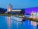 Fluss mit beleuchtetem Gebäude und Schiff am Ufer in der Abenddämmerung.
