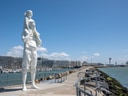 Grosse weisse Statue eines Mannes mit Kind auf den Schultern an einer Küstenpromenade mit Blick aufs Meer.