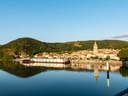Flusspanorama mit Dorf und Hügeln im Hintergrund.