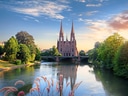 Kirche mit zwei Türmen an einem Fluss bei Sonnenuntergang.