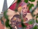 Wandgemälde einer Frau in Rüstung, teilweise verdeckt von Blättern, Kirchturm im Hintergrund.