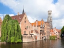 Historische Gebäude am Kanal in Brügge mit Turm im Hintergrund.