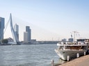 Flusskreuzfahrtschiff vor moderner Brücke und Skyline.
