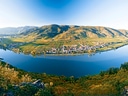 Panoramaansicht einer Flusslandschaft mit Hügeln und einem Dorf am Ufer.