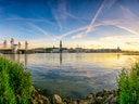 Panoramablick auf eine Flusslandschaft bei Sonnenuntergang mit Stadtansicht im Hintergrund.