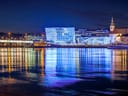 Nachtsicht einer beleuchteten Stadt am Fluss mit reflektierenden Lichtern im Wasser.
