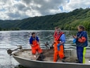 Menschen in orangefarbenen Overalls auf einem Boot auf einem See.
