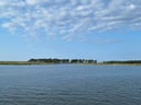 Weitläufiger Blick über ruhiges Wasser mit entfernter Baumreihe.