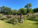 Person in einem Garten mit blühenden Sträuchern und Bäumen unter blauem Himmel.