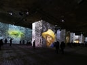 Menschen in einer Ausstellung mit grossflächigen Projektionen von Gemälden auf Wänden.