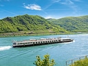 Flusskreuzfahrtschiff auf dem Rhein von grünen Hügeln umgeben.