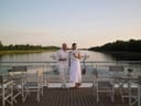 Zwei Personen auf einem Boot, umgeben von Wasser und Stühlen, bei Sonnenuntergang.
