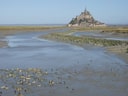 Blick auf eine felsige Insel mit einer grossen Struktur, umgeben von Wasser und Sand.