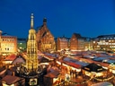 Weihnachtsmarkt mit beleuchteten Ständen und Kirche im Hintergrund.