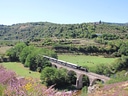 Dampfzug auf Eisenbahnbrücke in ländlicher Landschaft.