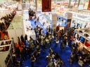 Menschenmenge auf einer Messe mit Ständen und blauen Teppichen.