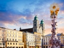 Barocke Säule auf Platz mit Kirche im Hintergrund bei Sonnenuntergang.
